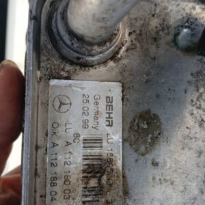 Close-up of a metal automotive part with a visible label containing the brand 'BEHR', 'Germany', and various alphanumeric codes, showing signs of dirt and wear.