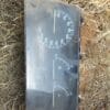 A dirty and cracked vehicle dashboard cluster showing a speedometer, fuel gauge, and temperature gauge, lying on dry grass and soil with a few rocks nearby.